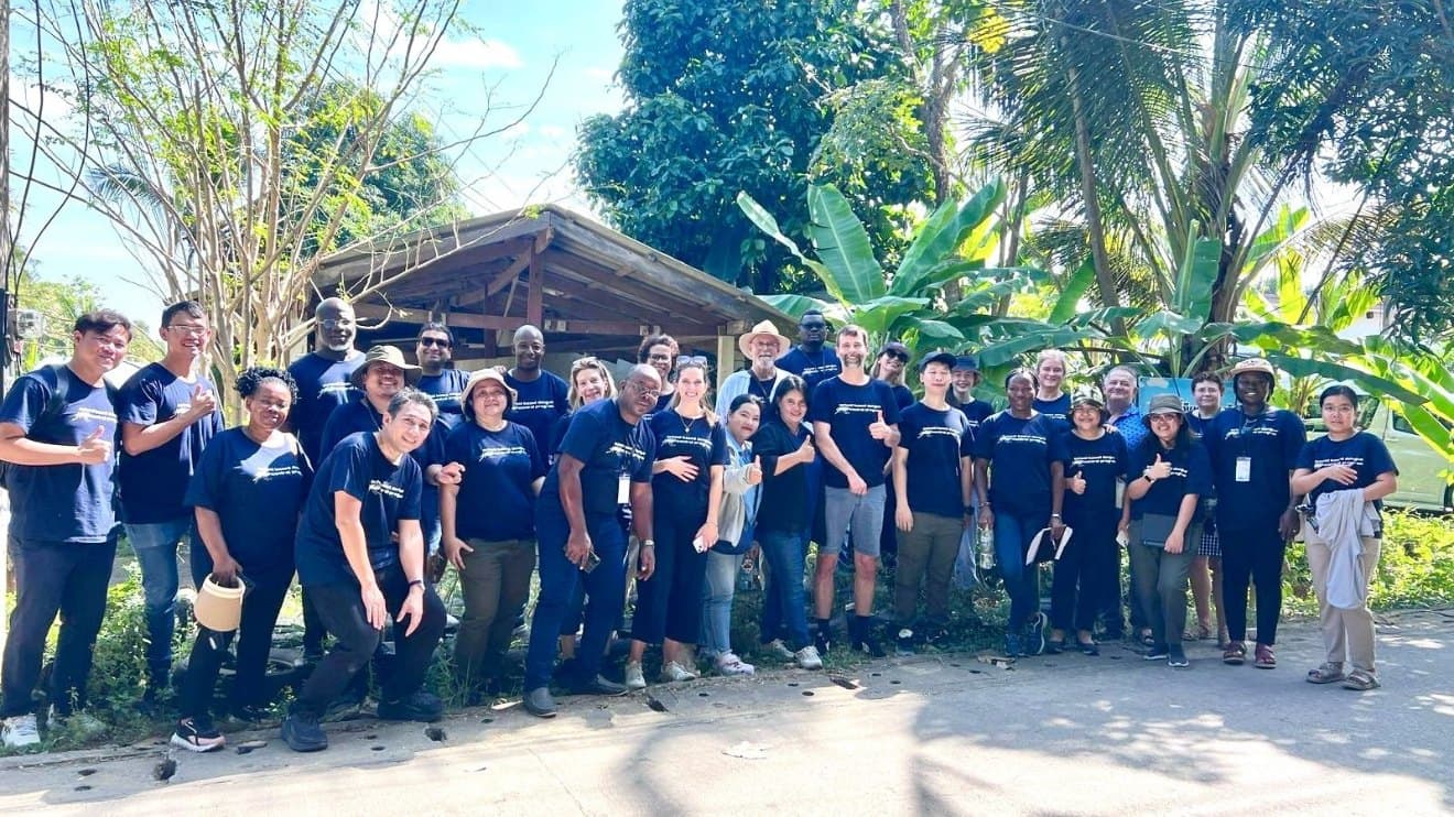 Groupe en t-shirts RAFT lors d'une visite de terrain, devant un abri en bois